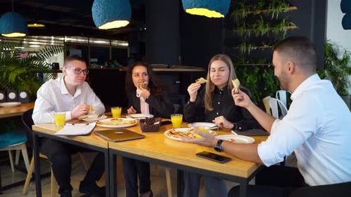 Office colleagues have lunch during break at work. Teammates enjoying pizza in a café at big table.