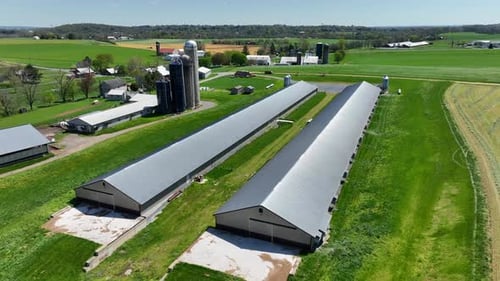 Aerial view of a large farm with long, modern barns, silos, and lush green fields in a rural landsca
