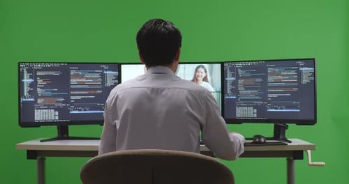 Rückansicht eines asiatischen Entwicklers, der Video hat, während er Code mit mehreren Bildschirmen auf grünem Bildschirm schreibt
