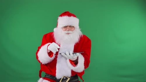 Santa Scrolls Through Tablet Against a Green Screen for Holiday Communication