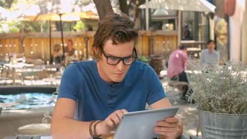 Young trendy student works on tablet computer at outdoor coffee cafe