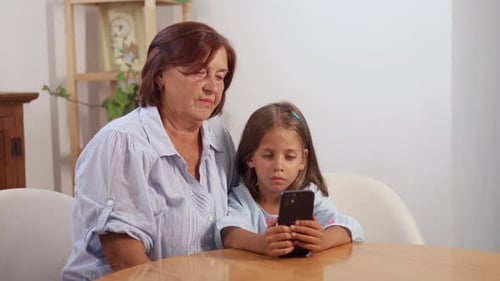 Grandmother and Girl Looking at Smartphone Together Indoors