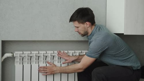 Man Sits Near Central Heating Radiator and Tries to Warm Up
