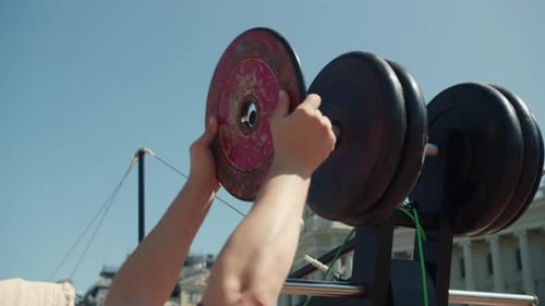 Male Hands Lift Metal Plates and Slide Onto Outdoor Barbell
