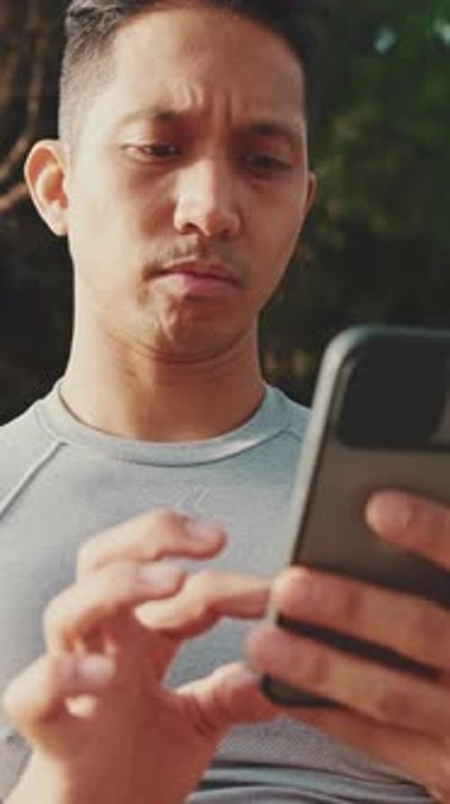 Young man sitting on a park bench uses a mobile phone