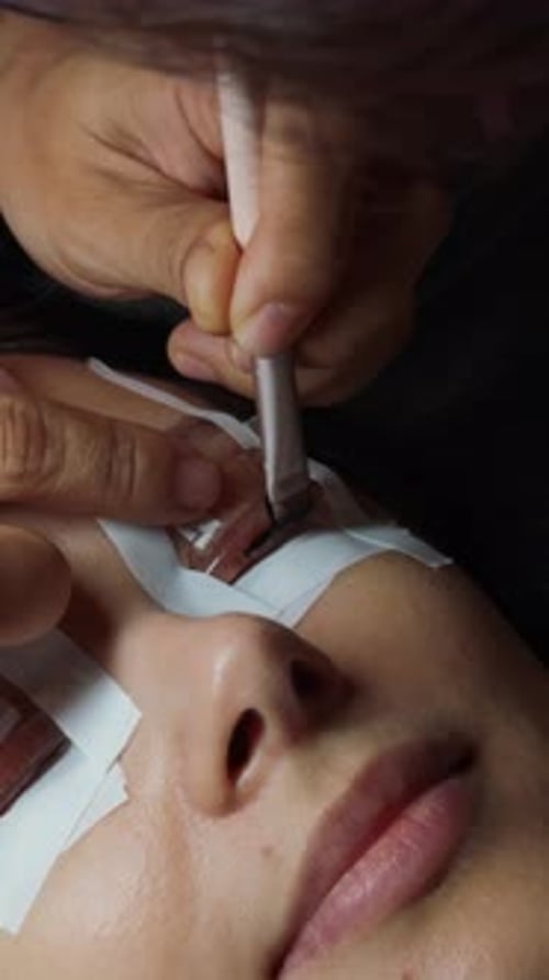 Mulher recebendo tratamento de aumento de cílios por um cosmetologista, com cuidado