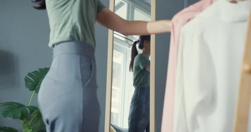 Senhora asiática escolhendo roupas no cabideiro se vestindo olhando no espelho na sala de estar em casa