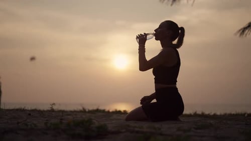 Woman Drinking Water on Tropical Beach at Sunset