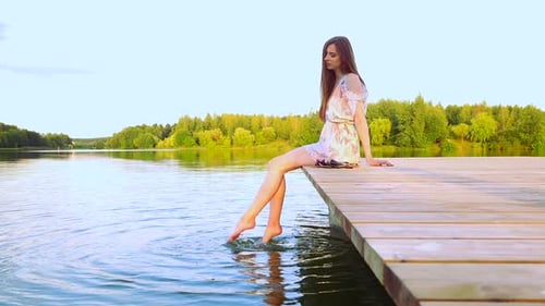 Carefree Woman Dangles Her Feet In The Water While Sitting On The Pier