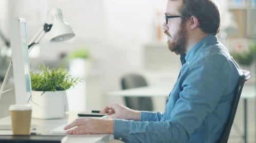 Young Bearded Man Working on Personal Computer while Sitting in His Creative Agency Office.