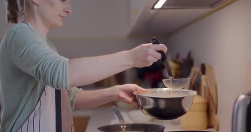 Frau schöpft beim Kochen in der Küche Pfannkuchenteig mit Schöpfkelle