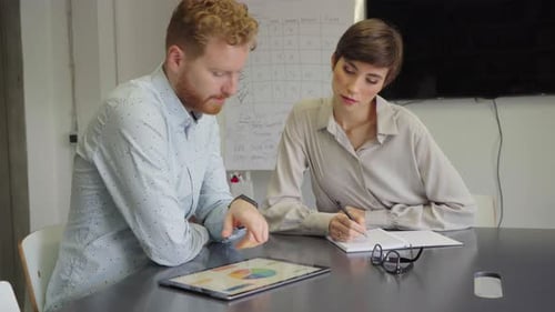 Man and woman collaborate on tablet at table