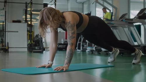 Fit Woman Doing Core Exercises in Plank Position on Mat at Gym