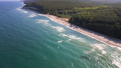 Aerial footage of a scenic sandy beach with waves gently hitting the shore, people relaxing under um