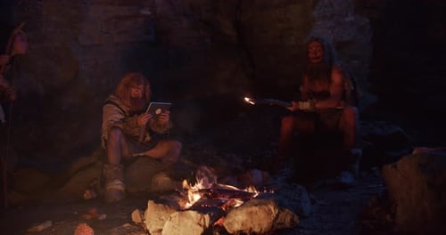 Cave Dwelling People Gather Around Fire in Rocky Cave