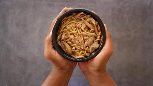 Hands Holding Bowl of Asian Noodles and Chicken