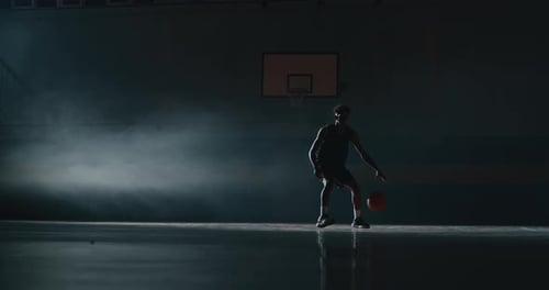 Basketball Player Dribbling in Dark Indoor Court