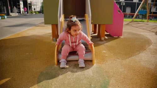 A Joyful Child in a Pink Outfit Explores a Vibrant Playground Enjoying the Thrill of Sliding Down