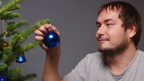 Man Decorating Christmas Tree with Blue Ornament