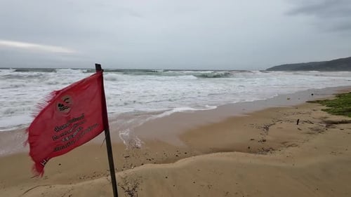 Rough Waves Crashing on Beach with Red Flag