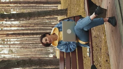 Freelance woman using laptop while sitting on bench in city park. Vertical video