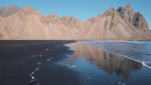 Black sand beach washed by sea waves below Vestrahorn mountain ridge.