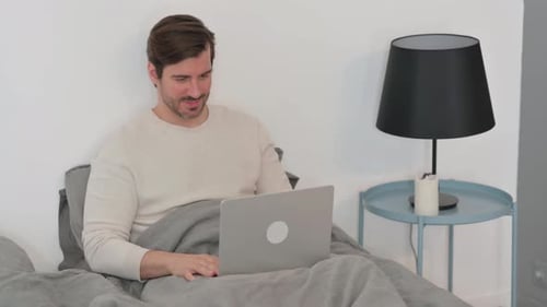 Online Video Chat on Laptop by Young Man Sitting in Bed