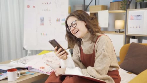 Smiling Young Woman Using Phone in Home Office
