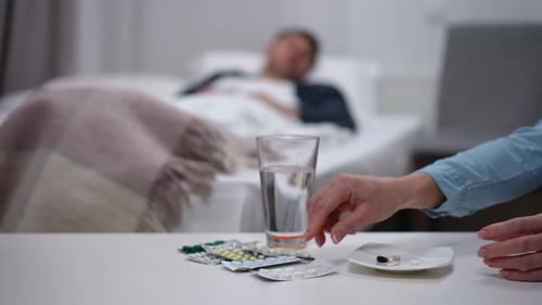 Woman Providing Pills to Man Lying in Bed
