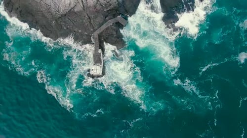 Aerial drone video of blue and green ocean sea water hitting the shoreline where steep cliffs and ro