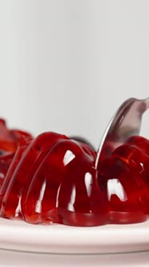 Vertical video. I break off a piece of red jelly with a spoon, cherries scattered on the plate.