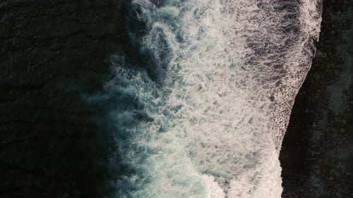 Aerial birds eye view of dramatic dark moody ocean water with white foaming waves breaking