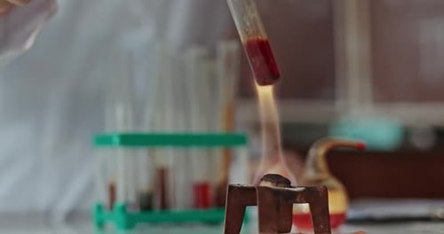 Unerkennbare Frau nimmt eine Röhre mit roter Substanz und legt sie beim Dirigieren über das Feuer