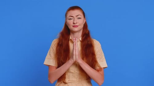 Woman Pleading with Hands Clasped on Blue Background