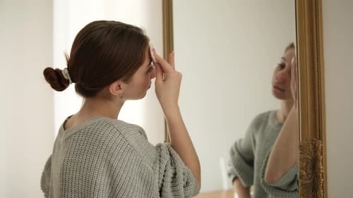 Young Woman Cleanses Face in Mirror at Home