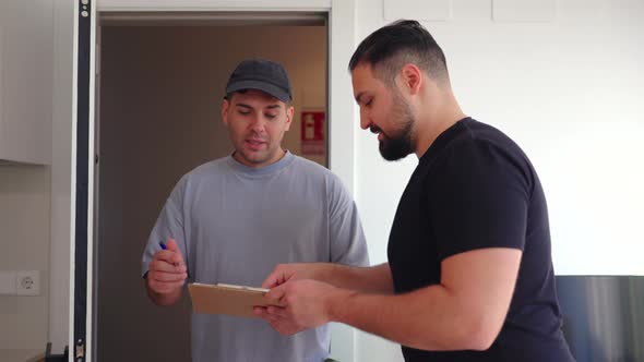 Man Signs Delivery Form for Another Man in Kitchen, Buildings Stock ...