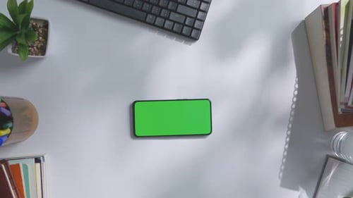Top down view of a mock up green screen smartphone on a white office desk