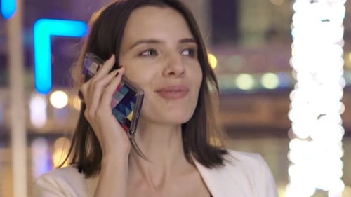 Junge, elegante Frau, die nachts in der Stadt in den 30ern mit dem Handy telefoniert