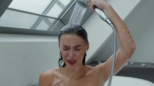 Woman rinsing dark hair under shower in bathroom