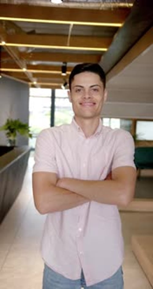 Vertical video: Smiling man standing with arms crossed in modern office hallway