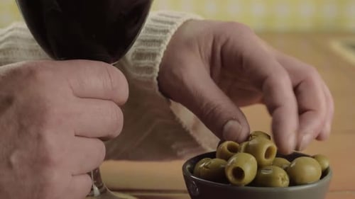 Hands holding glass of red wine eating green olives close up shot