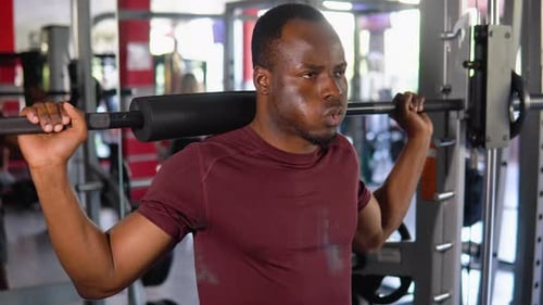 African American Bodybuilder Doing Squats Using a Barbell in a Gym to Train His Legs and Back