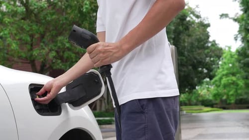 Progressive man install cable plug to his EV car from home charging station.