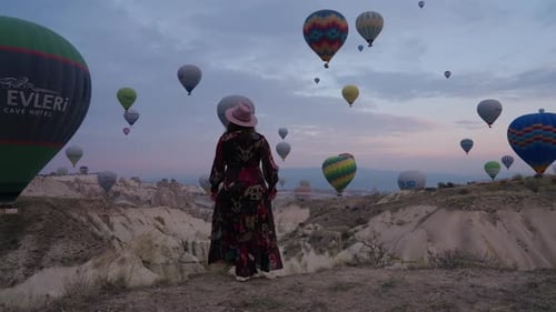 Young Girl In Dress Watching The Hotair Balloons Flying Over Cappadocia In Turkey. - rear