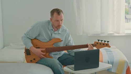 Man Playing Bass Guitar on Bed in Room