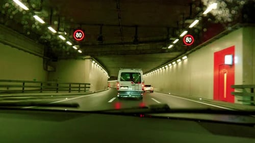 Driving through an automobile tunnel. Lights illuminate the tunnel where drivers are driving in thre