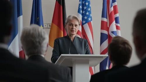 Woman Gives Speech at Podium Before Flags