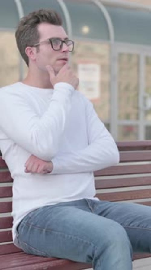 Pensive Young Man Thinking while Sitting Outdoor on Bench, Vertical Video