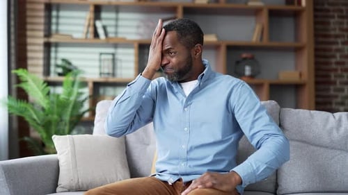 Mature african american man is hot while sitting on sofa in living room at home. Senior bearded male