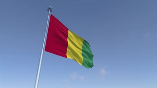 Guinea Flag Waving on Flagpole Against Blue Sky